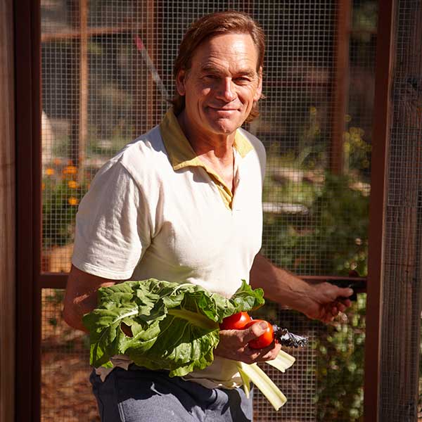 Darin Olien looking toward the camera with freshly picked garden vegetables
